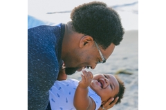 Image A man holds a beautiful, laughing baby at the beach.